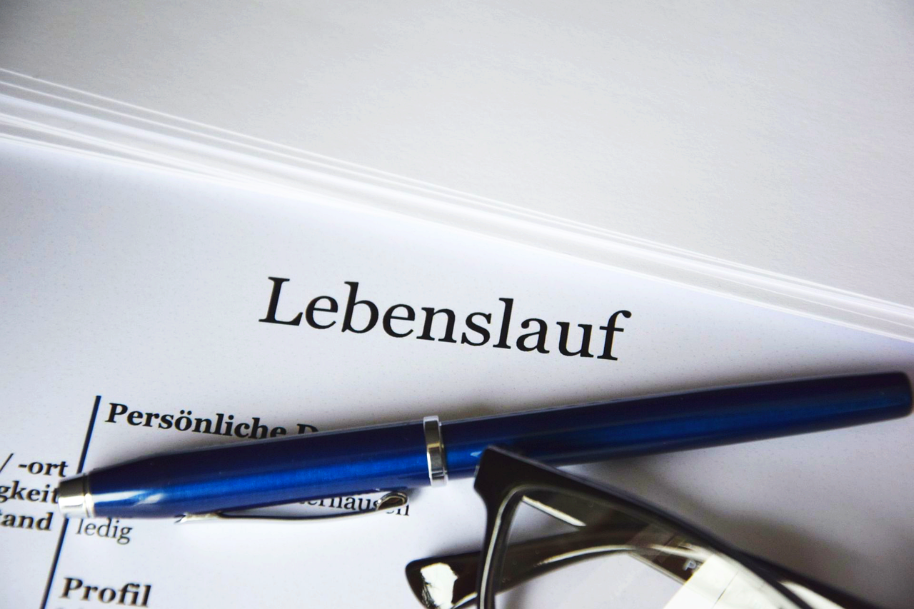 Sie sehen den Schriftzug "Lebenslauf" auf einem Blatt Papier mit mehreren Stiften daneben.