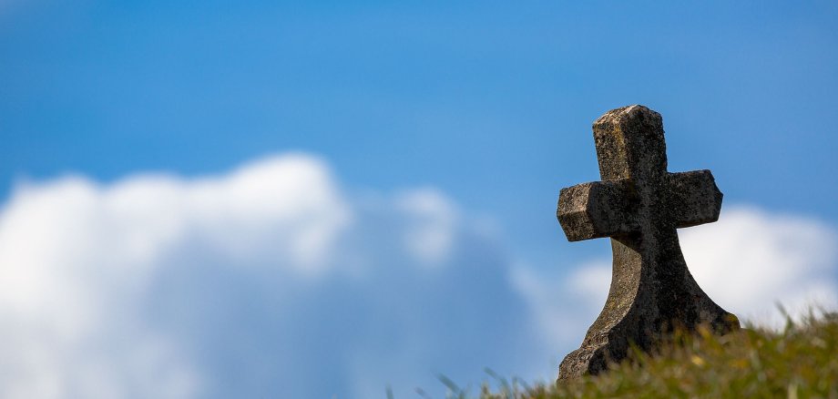 Sie sehen einen Grabstein auf einer grünen Wiese und blauem Himmel.