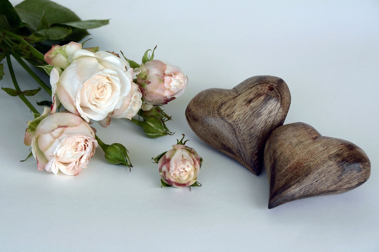 Hier sehen Sie weiße Rosen und zwei Holzherzen als hochzeitliche Dekoration.