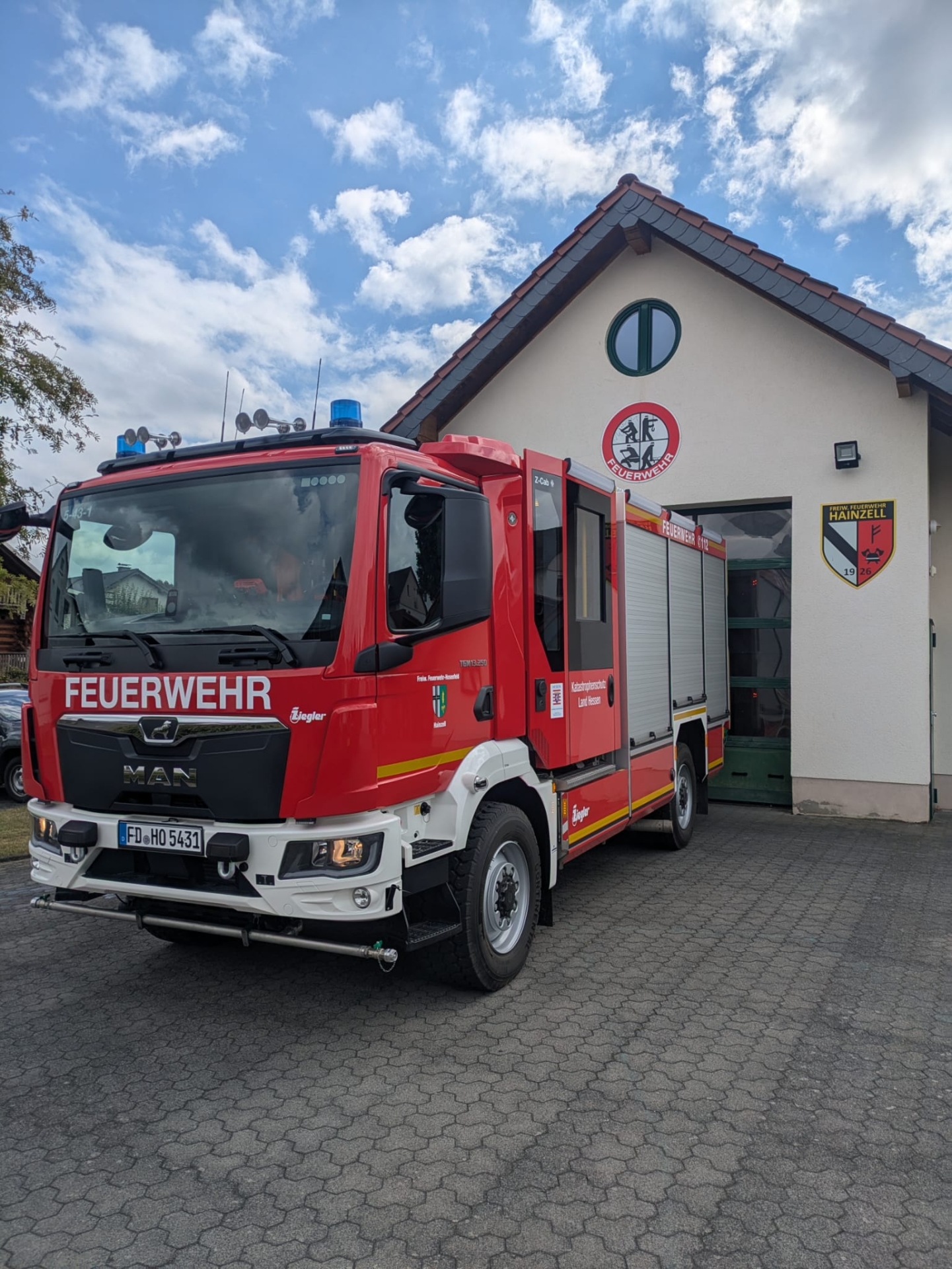 Hier sehen Sie das Feuerwehrhaus in Hainzell mit Feuerwehrauto davor.