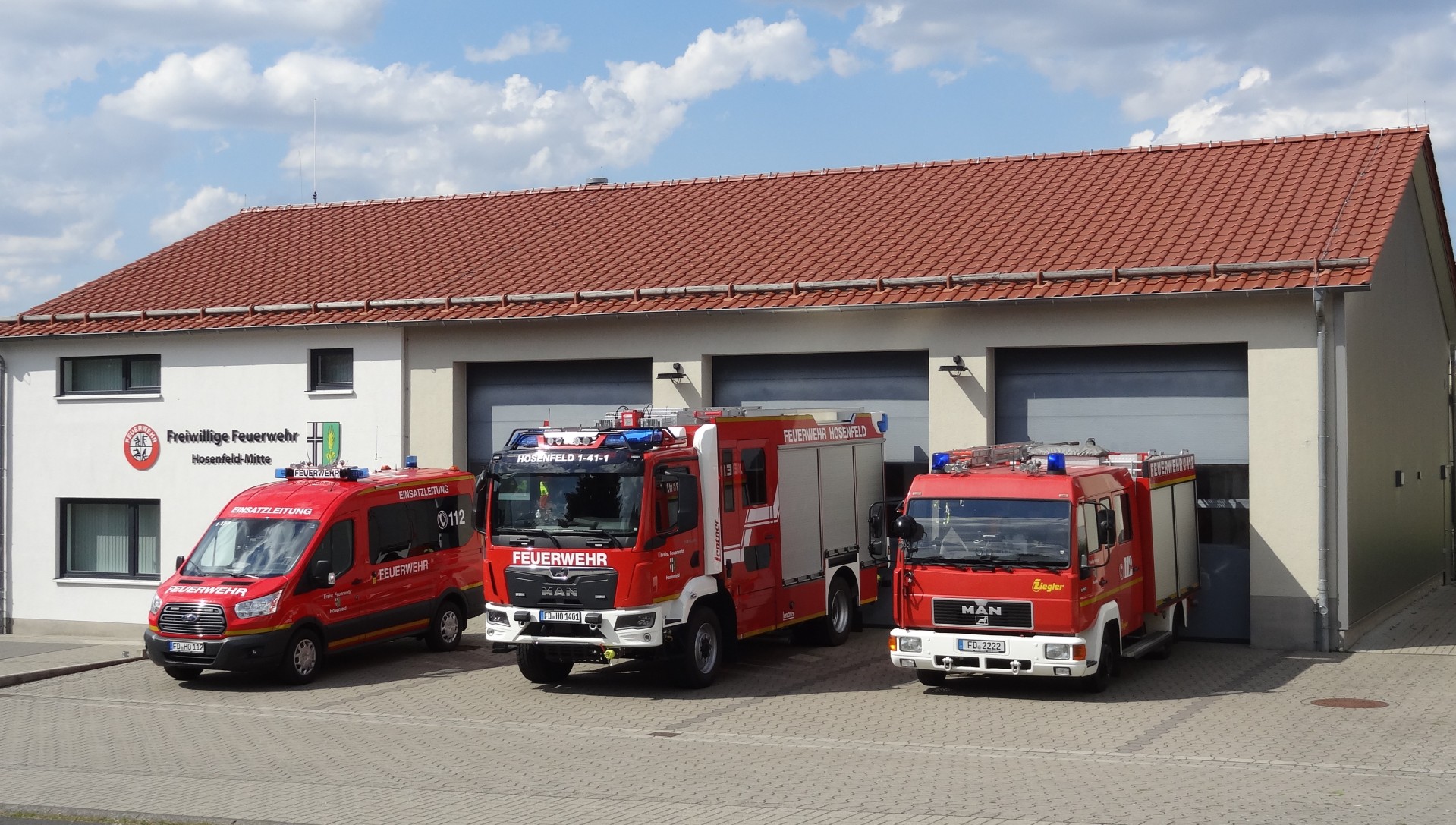 Feuerwehrhaus Hosenfeld Sie sehen das Feuerwehrhaus Hosenfeld mit drei Feuerwehrfahrzeugen davor.