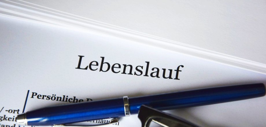 Sie sehen den Schriftzug "Lebenslauf" auf einem Blatt Papier mit mehreren Stiften daneben.